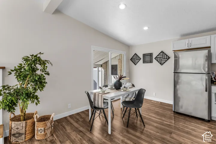 Wood-finish flooring, vaulted ceiling, recessed lighting, white cabinetry, stainless steel refrigerator