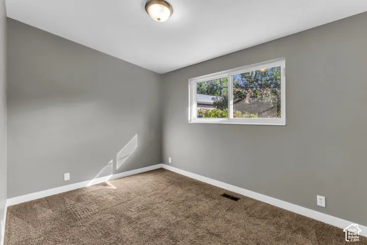 Bright corner bedroom featuring neutral gray walls, soft white ceiling trim, and neutral-toned carpet flooring