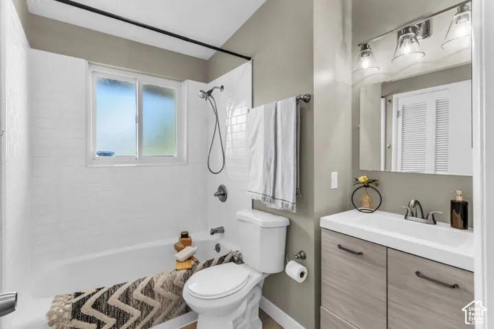 Main bathroom with a Laundry Chute! White subway tile shower surround with a window, single vanity with wood-finish cabinetry, and a chrome-finish faucet