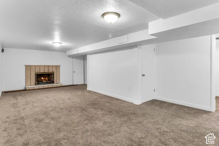 Spacious basement recreation area featuring neutral carpet flooring, recessed ceiling lighting, and a brick fireplace with wood mantel