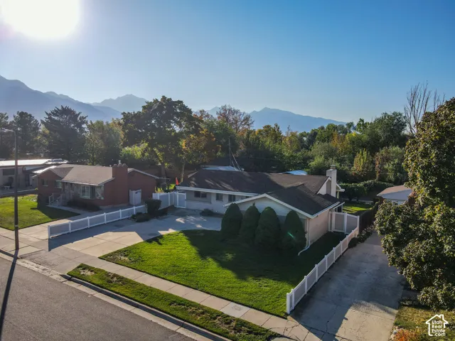 Mountain backdrop, mature trees, manicured lawn, paved driveway, white privacy fencing