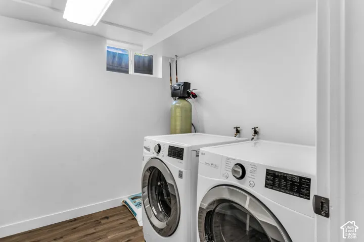 Laundry area featuring wood-finish flooring, white walls, and a window and water softner.