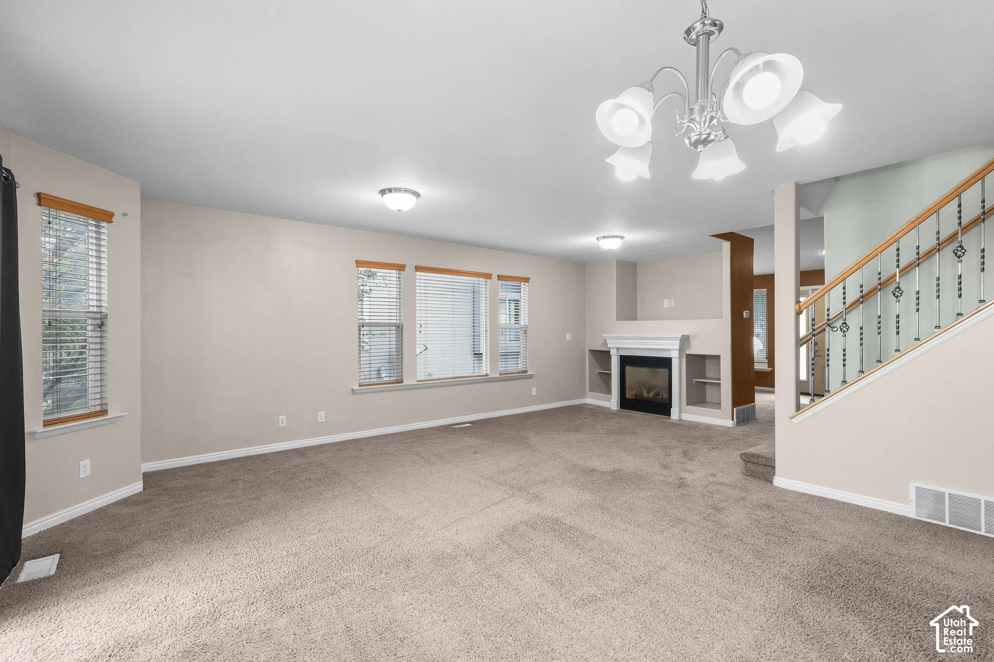 Spacious living area featuring neutral-toned carpeting, multiple windows, a decorative fireplace with a white mantel, and built-in shelving