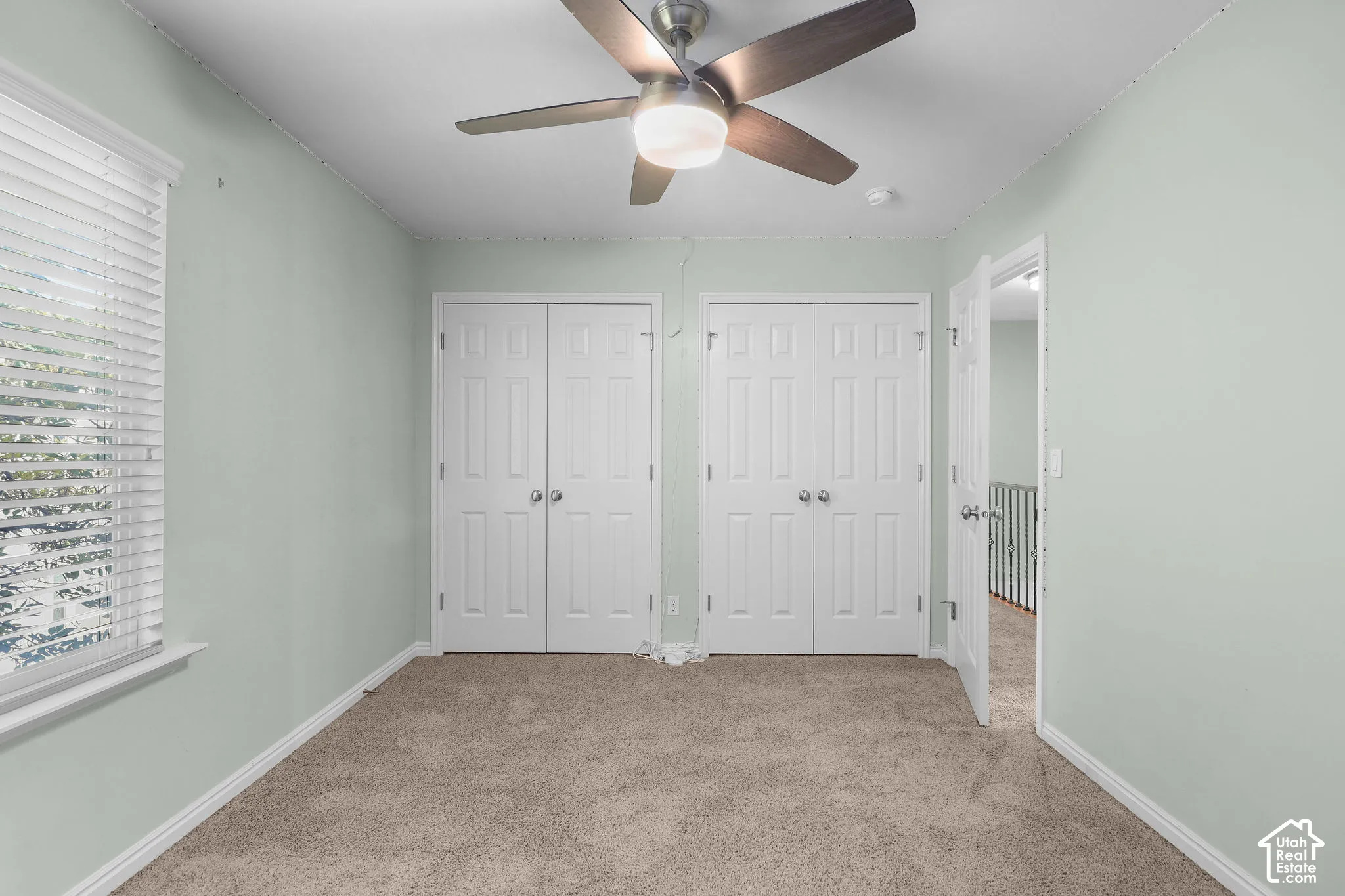 Ceiling fan with integrated lighting, two sets of bi-fold closet doors, wall-to-wall carpeting, window with horizontal blinds, and a paneled interior door
