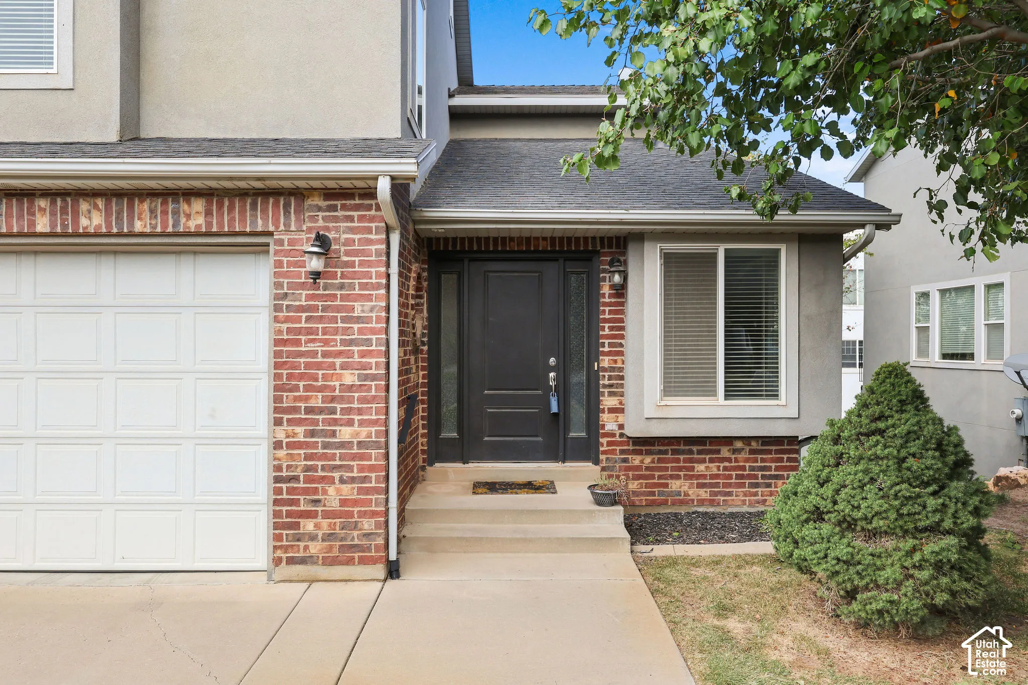 Brick and stucco exterior with an attached garage, covered entryway, and mature landscaping