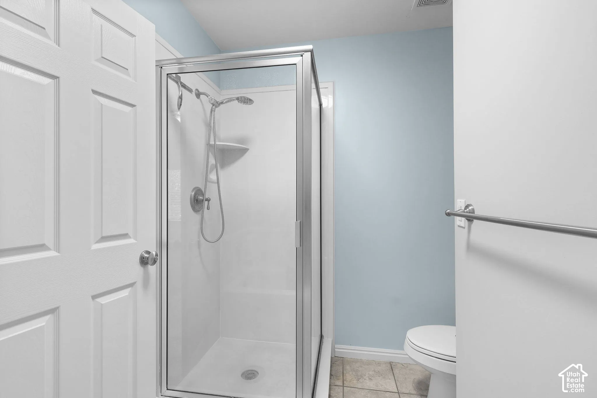 Glass-enclosed shower with a multi-function showerhead, white panel door, and neutral tiled flooring