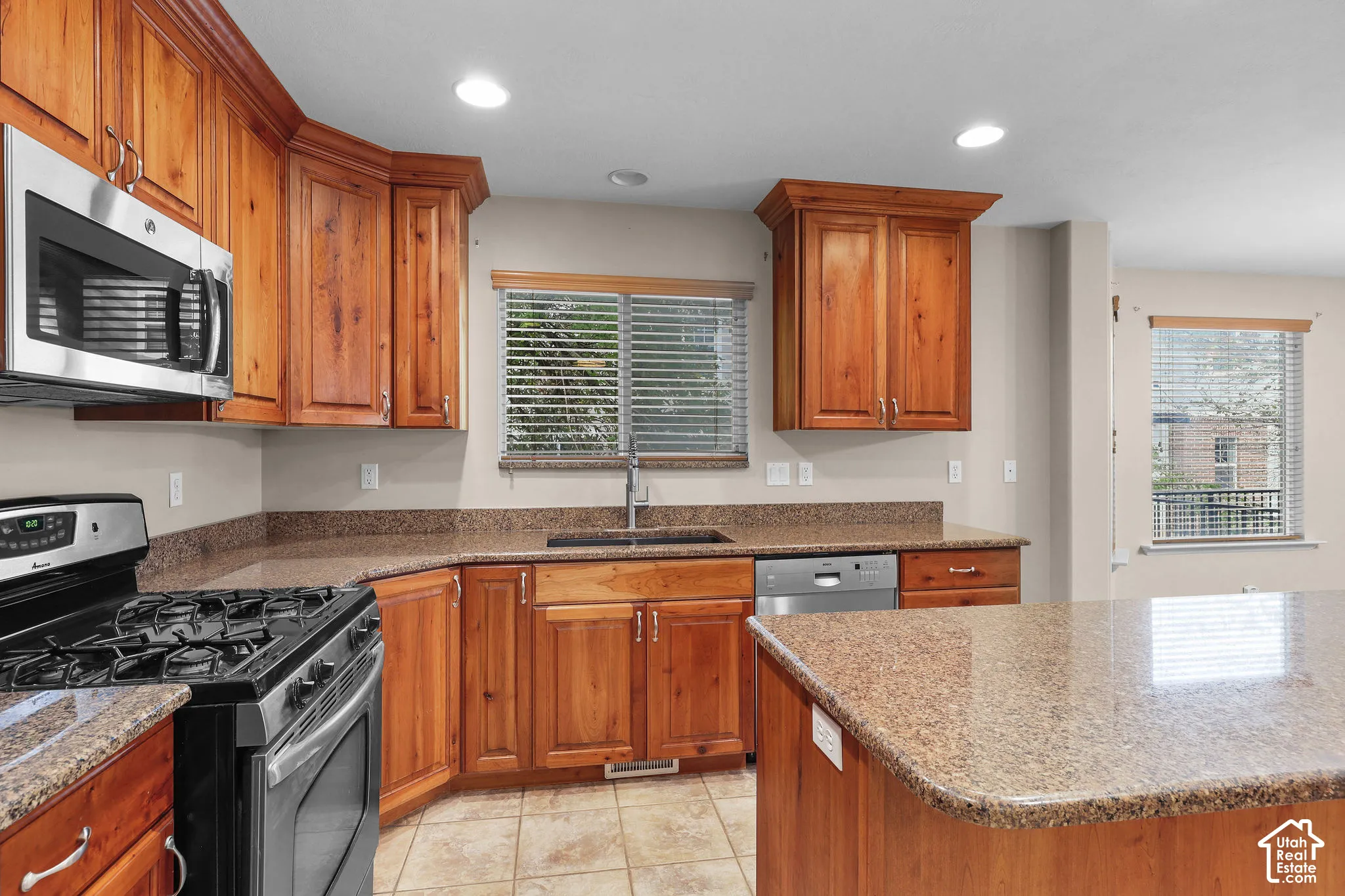 Kitchen featuring wood cabinetry, stainless steel appliances, speckled countertops, a built-in sink, and tile flooring