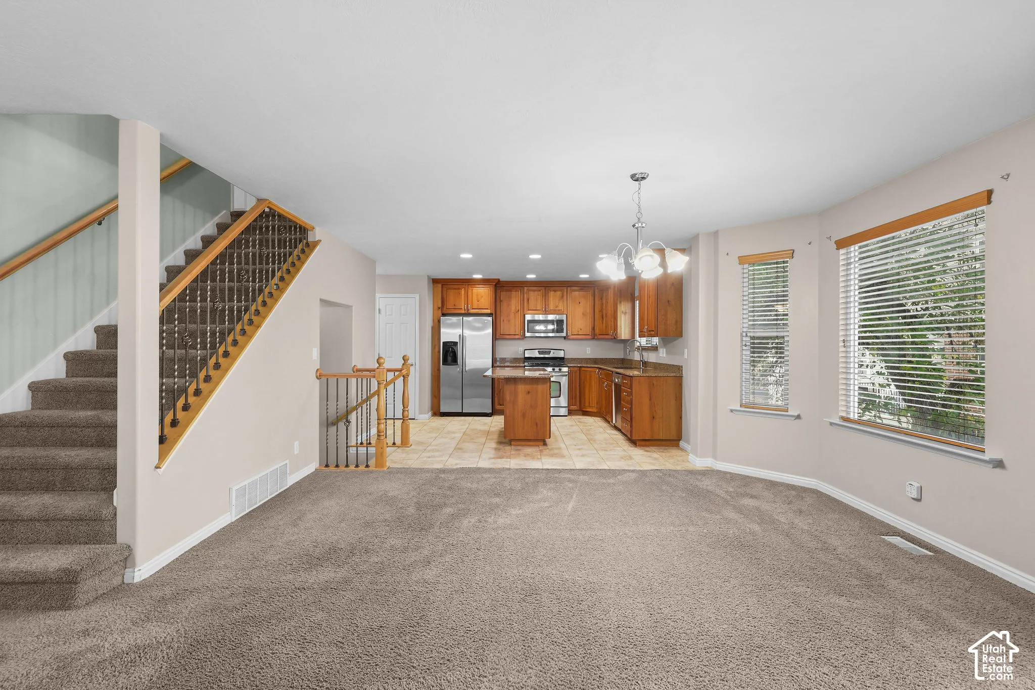Open-concept living space with warm wood-finish cabinetry, stainless steel appliances, and a chandelier fixture