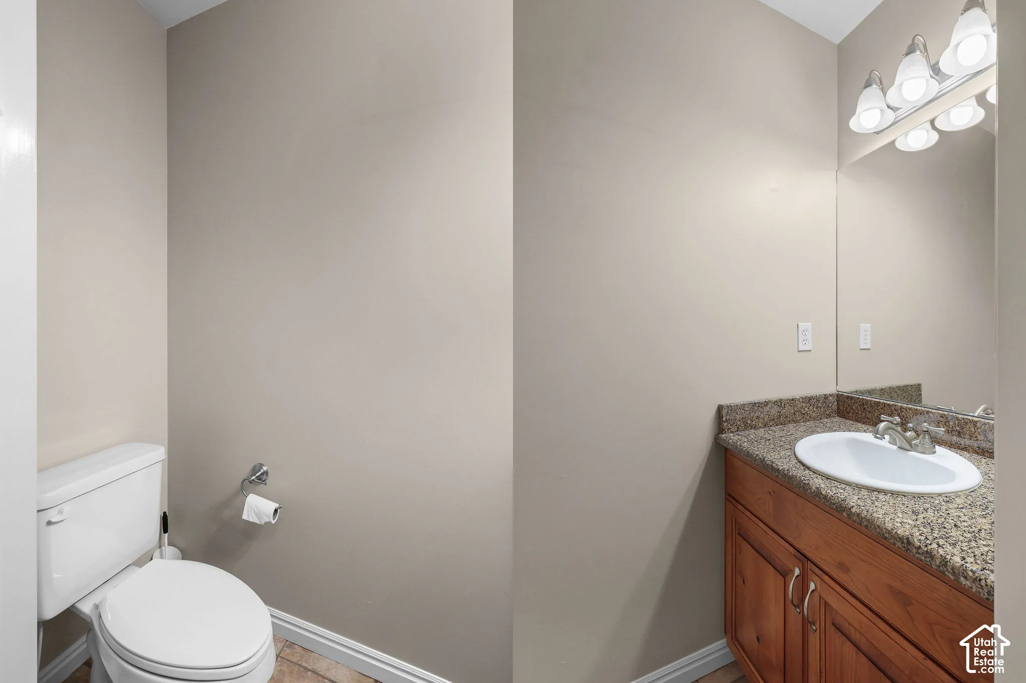 Wood-finish flooring with a white toilet, chrome toilet paper holder, wood vanity, integrated sink, and a speckled countertop