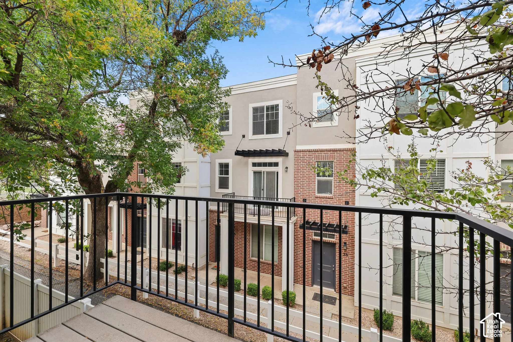 Balcony with black metal railing, featuring a multi-story exterior with brick and stucco finishes, and a dark entry door