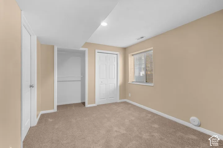 Carpeted room featuring a window with blinds, recessed lighting, and multiple doors