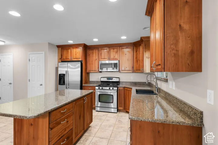 Kitchen featuring wood-finish cabinetry, stainless steel appliances, granite countertops, a kitchen island, and recessed lighting