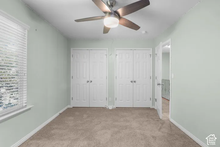 Ceiling fan with integrated lighting, two sets of bi-fold closet doors, wall-to-wall carpeting, window with horizontal blinds, and a paneled interior door