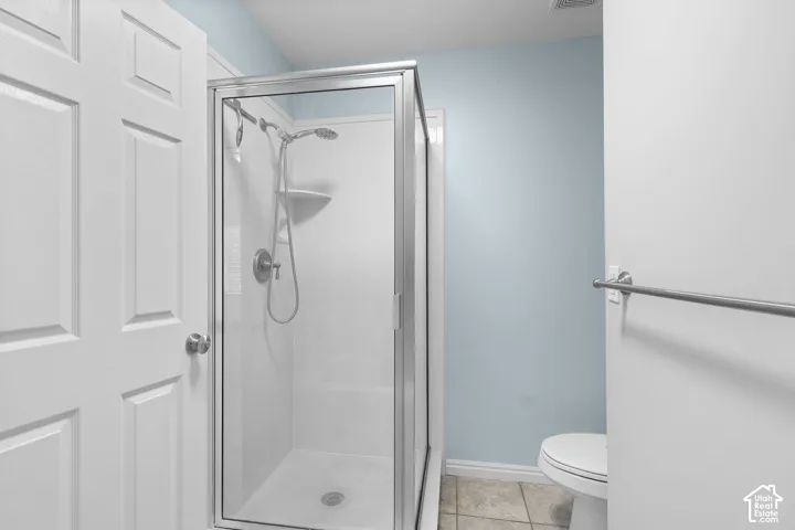 Glass-enclosed shower with a multi-function showerhead, white panel door, and neutral tiled flooring