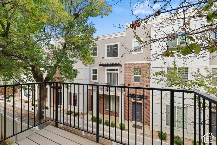 Balcony with black metal railing, featuring a multi-story exterior with brick and stucco finishes, and a dark entry door