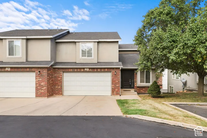 Stucco exterior with brick accents, attached garage, prominent front entry, and mature tree