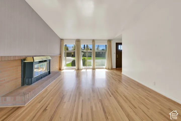 Expansive living area featuring wood-finish flooring, a brick fireplace with a metal insert, and multiple large windows