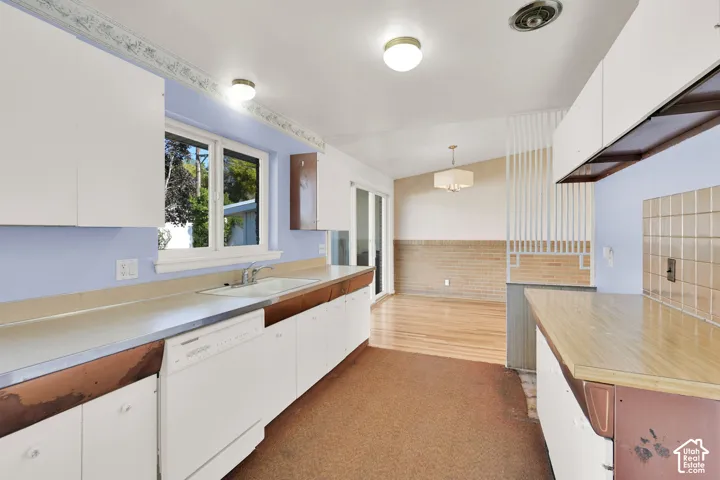 Kitchen with white cabinetry, light-toned countertops, integrated dishwasher, and a window above the sink