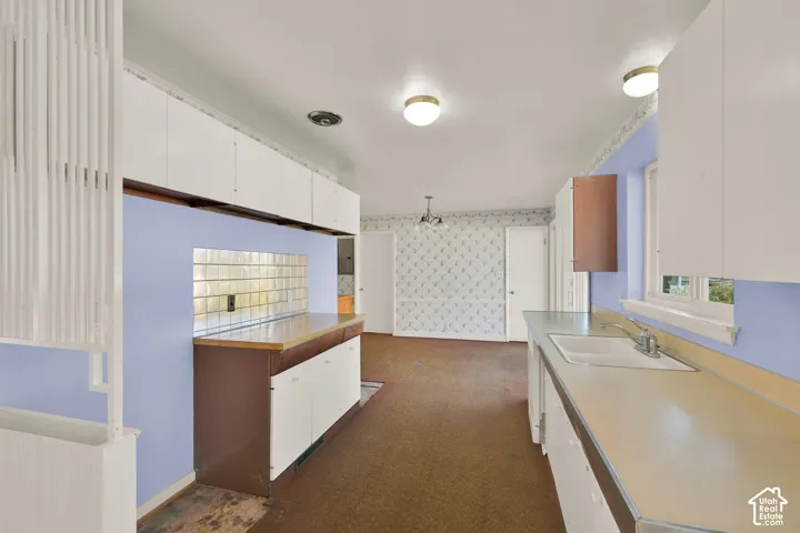 Kitchen featuring white upper cabinetry, light-colored countertops, a single basin sink, and glass block detailing
