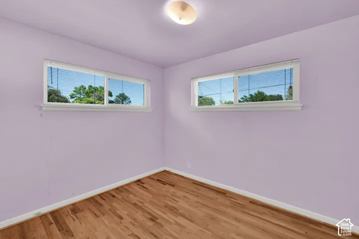 Hardwood flooring, two windows with blinds, white trim, and a ceiling-mounted light fixture
