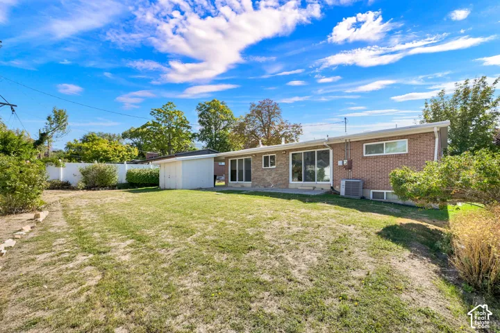 Expansive backyard with a manicured lawn, a white privacy fence, and a brick-sided home with sliding glass doors