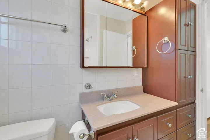 Vanity with integrated sink and chrome fixtures, framed mirror with overhead lighting, built-in cabinetry, tiled walls, and adjacent toilet
