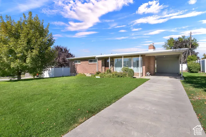 Brick exterior with a covered carport, expansive front lawn, mature tree, and a concrete driveway