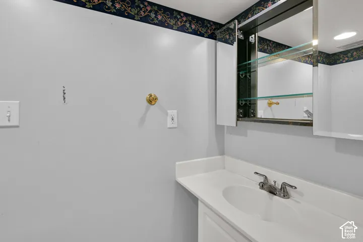 Vanity with integrated sink, chrome faucet, and mirrored medicine cabinet with glass shelving