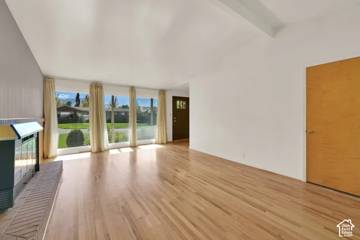 Hardwood flooring, vaulted ceiling, large picture windows, wood-burning fireplace with brick hearth, and a dark wood entry door