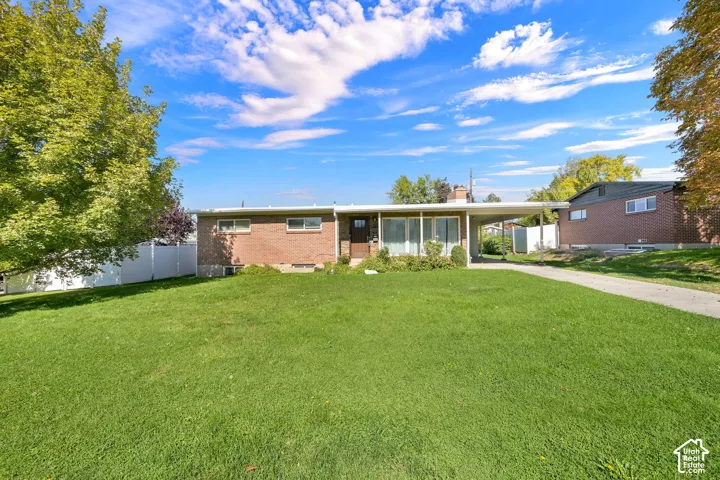 Brick exterior with a covered carport, mature trees, a manicured lawn, and a paved driveway