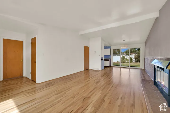 Hardwood flooring throughout, vaulted ceiling, exposed beam, sliding glass patio doors, and a built-in fireplace