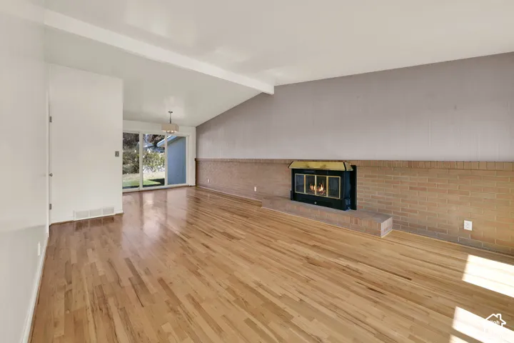 Wood-finish flooring, vaulted ceiling, brick fireplace with metal insert, and sliding glass doors