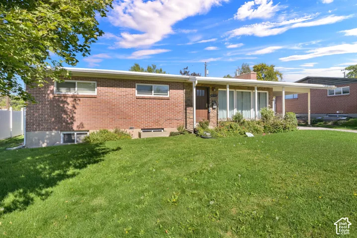 Brick ranch home with expansive manicured lawn, mature shade trees, and open grounds