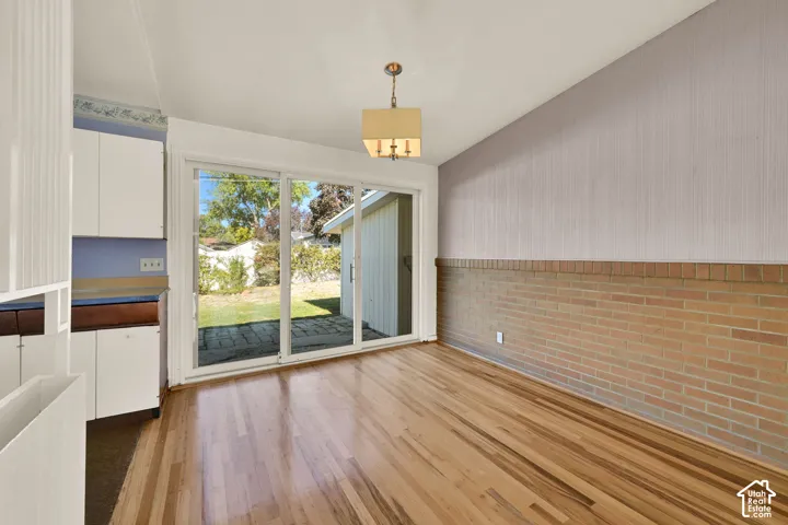 Hardwood flooring, brick accent wall, white cabinetry, sliding glass door, and a built-in light fixture