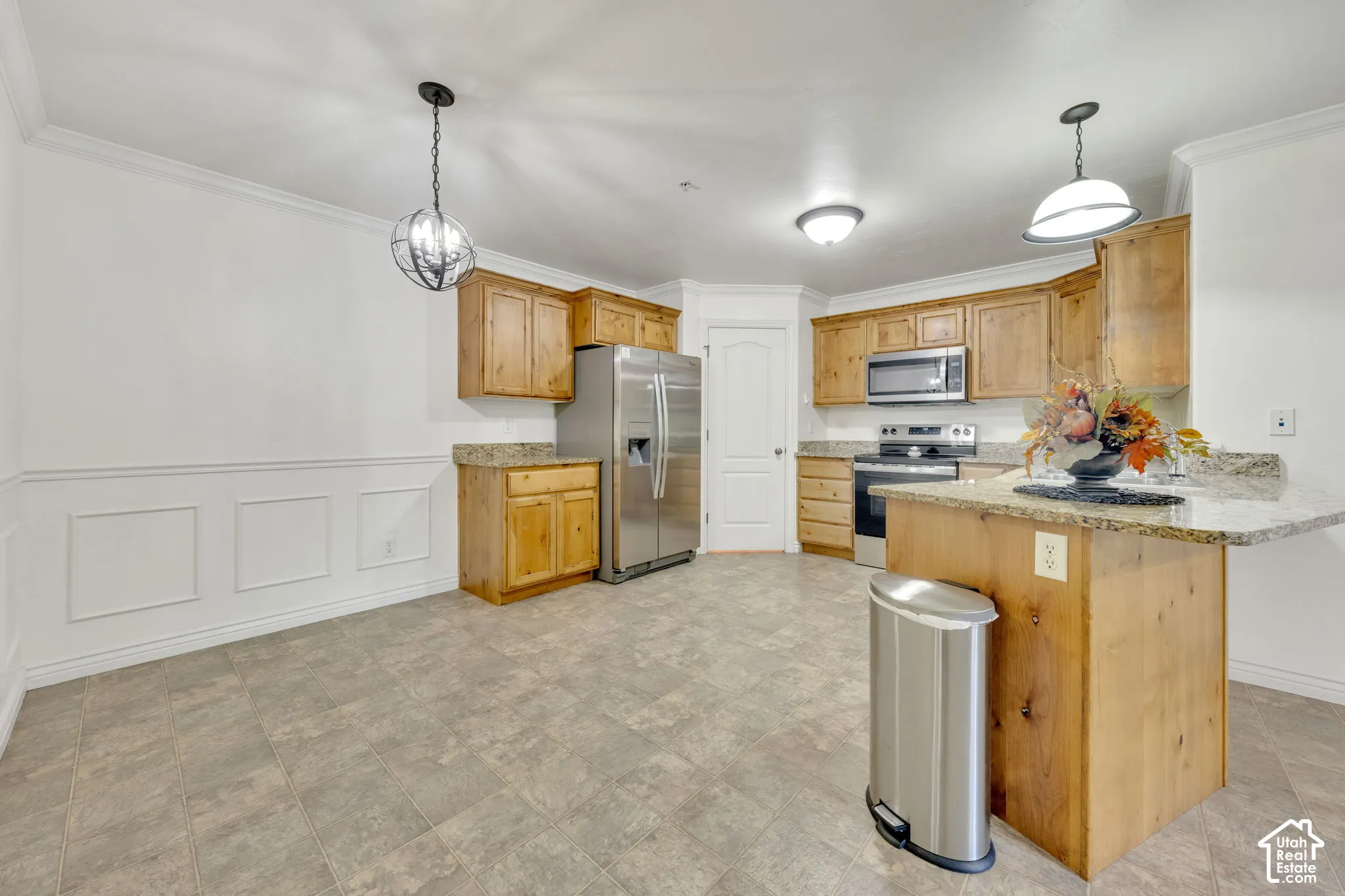 Kitchen featuring wood cabinetry, stainless steel appliances, granite countertops, tile flooring, and wainscoting