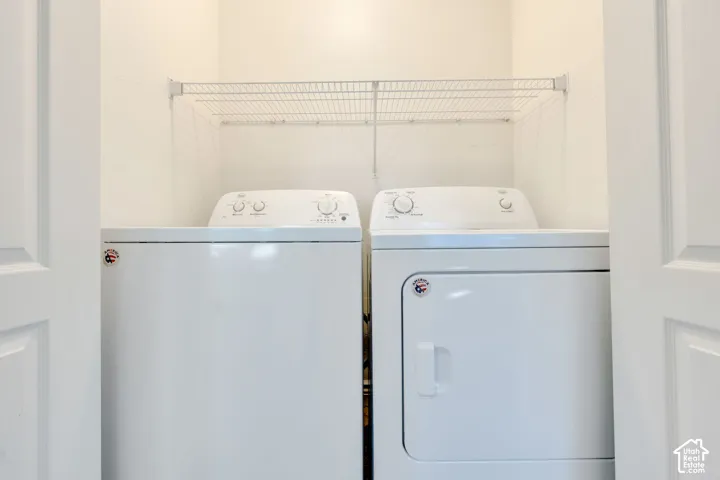 White laundry appliances within a dedicated closet featuring a wire storage shelf
