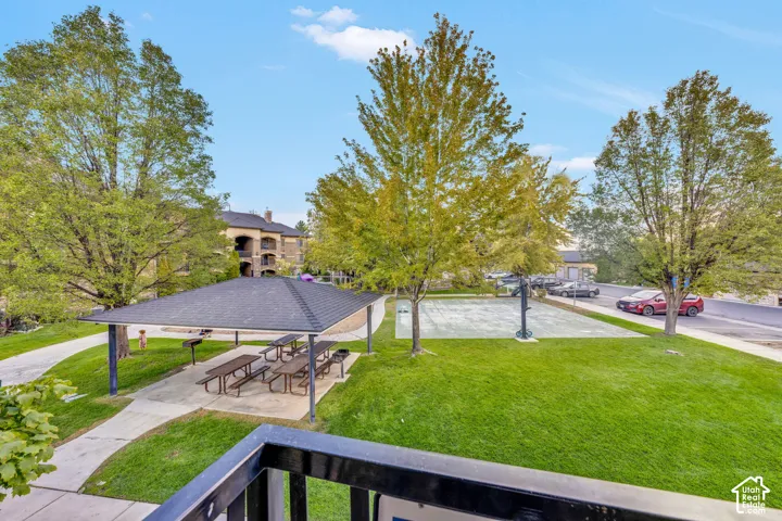 Manicured lawn with mature trees, covered picnic area with multiple tables, paved walkway, and a basketball court