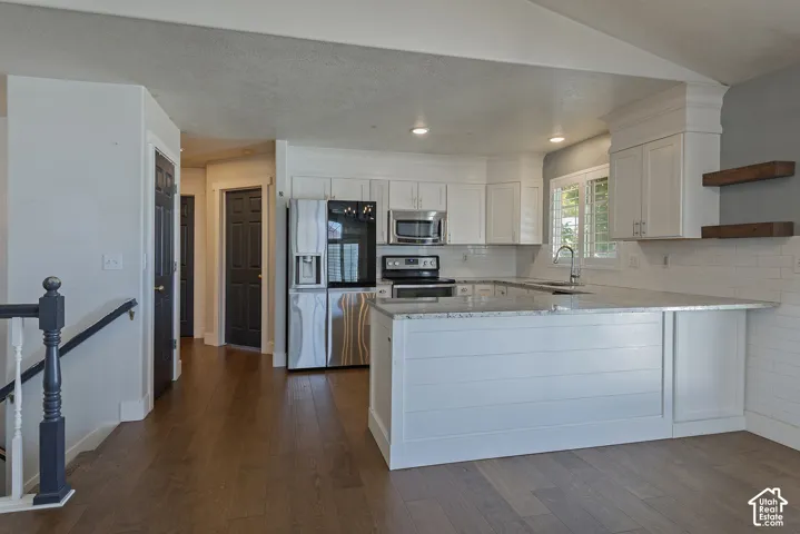 Open-concept kitchen featuring white shaker cabinetry, stainless steel appliances, a center island with bar seating, wood-finish flooring, and a subway tile backsplash
