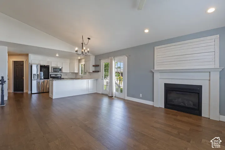 Open-concept living space with wood-finish flooring, a white kitchen with stainless steel appliances, a built-in fireplace with a mantel, and French doors