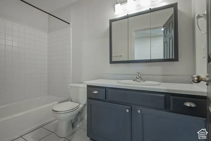 Bathroom featuring a white subway tile tub surround, dark gray vanity with chrome hardware, white countertop with an integrated sink, and a mirrored medicine cabinet with vanity lighting