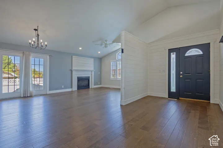 Spacious open-concept living area featuring hardwood flooring throughout, abundant natural light from French doors and transom windows, decorative chandelier, gas fireplace with white mantel surround, and a dramatic vaulted ceiling with ceiling fan