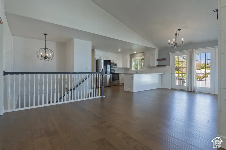 Wood-finish flooring, white spindle railing with dark handrail, vaulted ceiling, white kitchen cabinetry with stainless steel appliances, and French doors