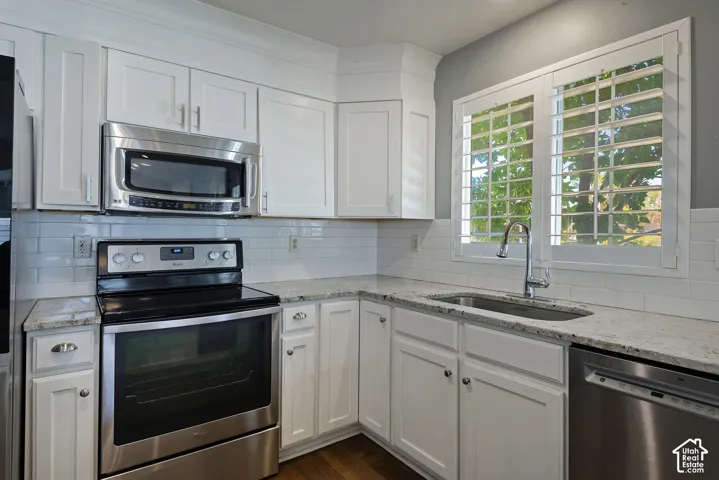 White cabinetry, subway tile backsplash, stainless steel appliances, light-toned countertops, and plantation shutters