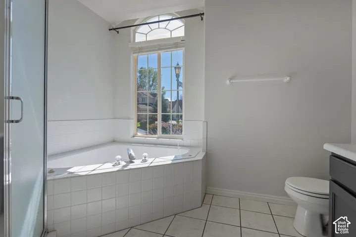 Soaking tub with tiled surround, arched window, glass shower enclosure, and tiled flooring