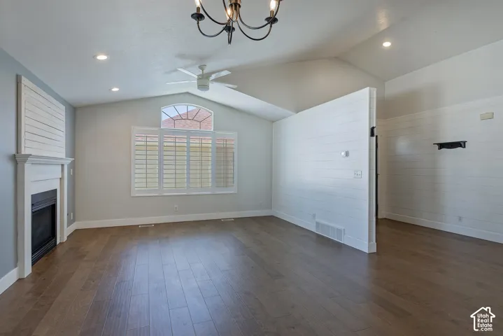 Vaulted ceiling with a ceiling fan, fireplace with a white mantel, wood-finish flooring, recessed lighting, and a window with plantation shutters