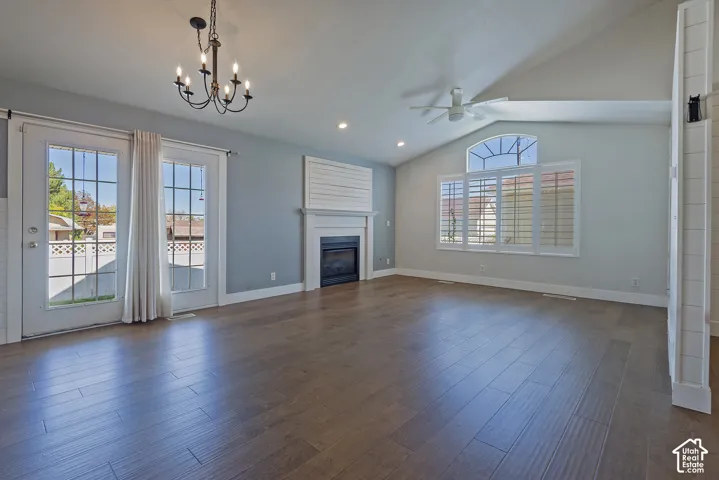 Vaulted ceiling with a ceiling fan, wood-finish flooring, two French doors, a fireplace, and a large window with plantation shutters