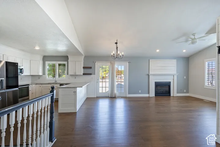 Open-concept living area featuring wood-finish flooring, a white-mantled fireplace, and a kitchen with white cabinetry and stainless steel appliances