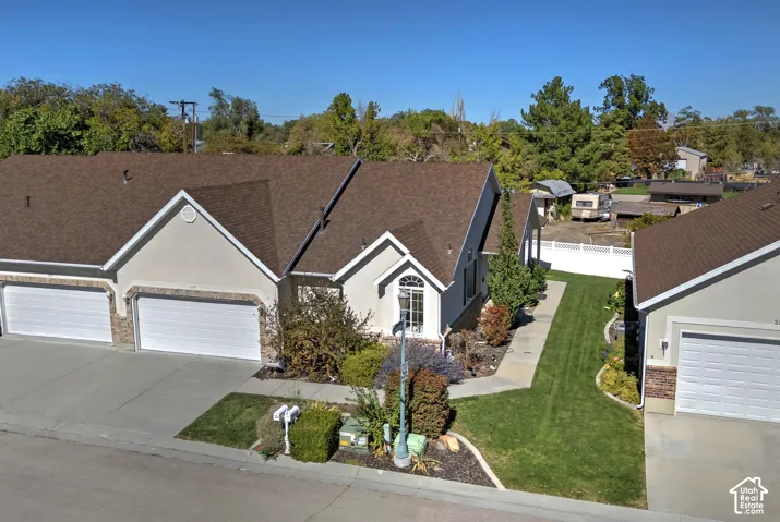 Multi-level brown shingle roofline, stucco exterior with stone accents, two-car garage, arched window, and mature landscaping