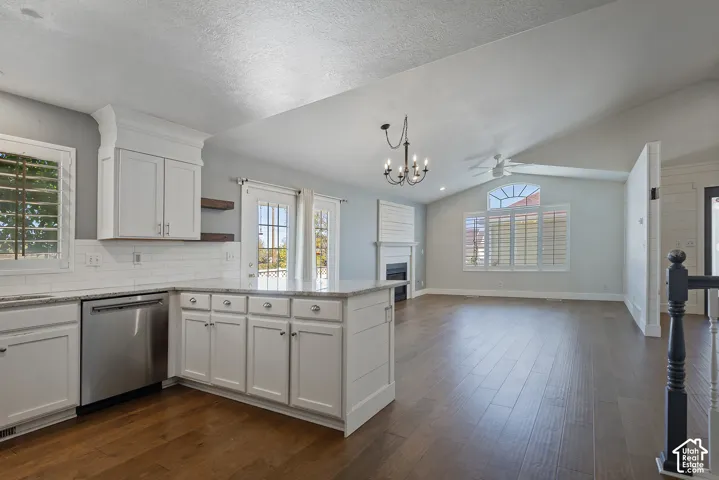White cabinetry with granite countertops, stainless steel dishwasher, wood-finish flooring, and a vaulted ceiling with a fireplace