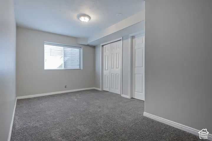 Grey carpeted flooring, light grey painted walls, white trim, a double bi-fold closet, and a single window with white blinds